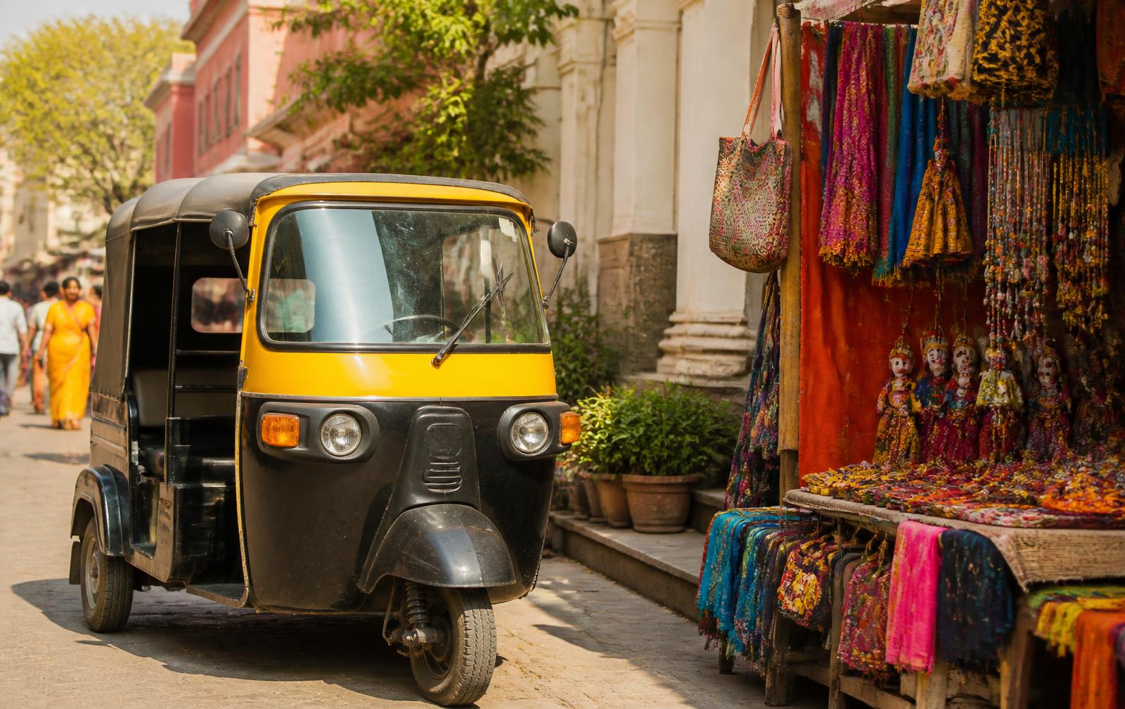 A yellow and black auto rickshaw parked beside a colorful Indian street market stall